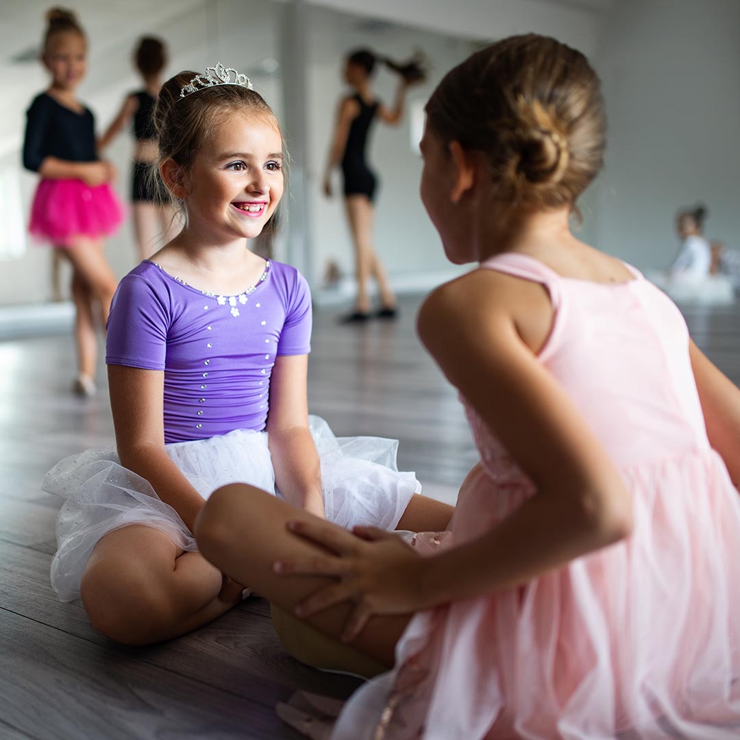 Two girls in dance class smiling and talking to each other